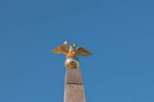 A golden eagle statue perched on a monument with a vivid blue sky background