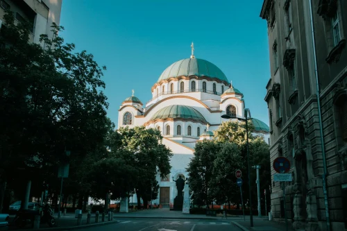 View of the iconic Saint Sava Temple in Belgrade on a sunny day, framed by trees and buildings