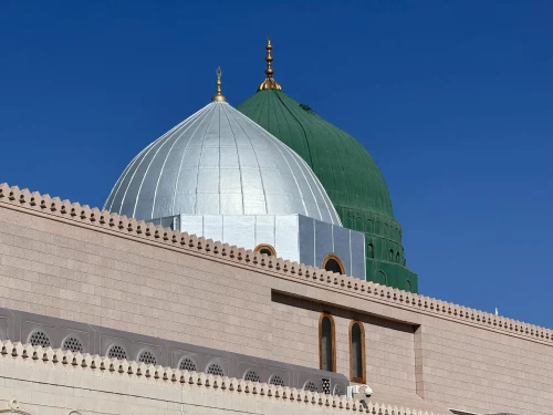 The iconic green and silver domes of Masjid Nabawi under a clear blue sky in Madinah, Saudi Arabia