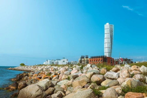 Iconic Turning Torso tower beside a rocky coastline in Malmö, with a clear blue sky