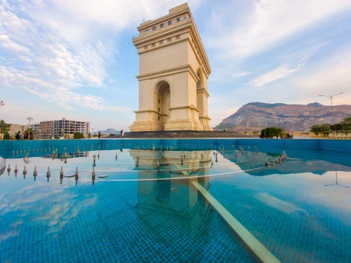 Beautiful arch monument with a reflecting pool under a bright blue sky, set against a mountain backdrop