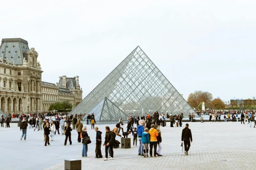 Tourists gather around the iconic Louvre Pyramid in Paris, highlighting European architecture