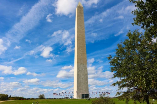 Stunning photo of the Washington Monument against a vibrant blue sky with clouds, surrounded by green grass
