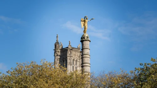 The golden statue atop a column near the iconic Tour Saint-Jacques under a clear blue sky in Paris