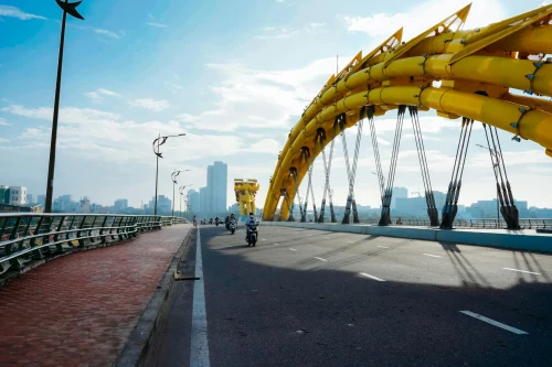 Motorcycles cross the iconic yellow Dragon Bridge in Da Nang under a clear blue sky