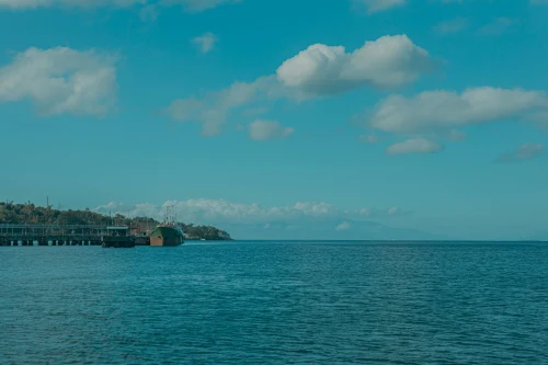 A serene coastal scene with a pier and moored ship under a bright blue sky